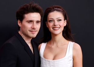 Brooklyn Beckham in a black suit and Nicola Peltz in a white dress at an event