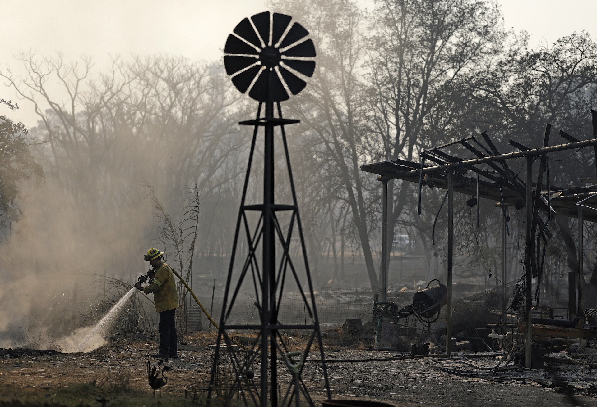 a fireman sprays water on smoldering bushes around burned structures