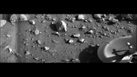A black-and-white image of the surface of Mars with rocks and part of the Viking 1 lander. 