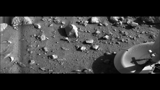 A black-and-white image of the surface of Mars with rocks and part of the Viking 1 lander. 