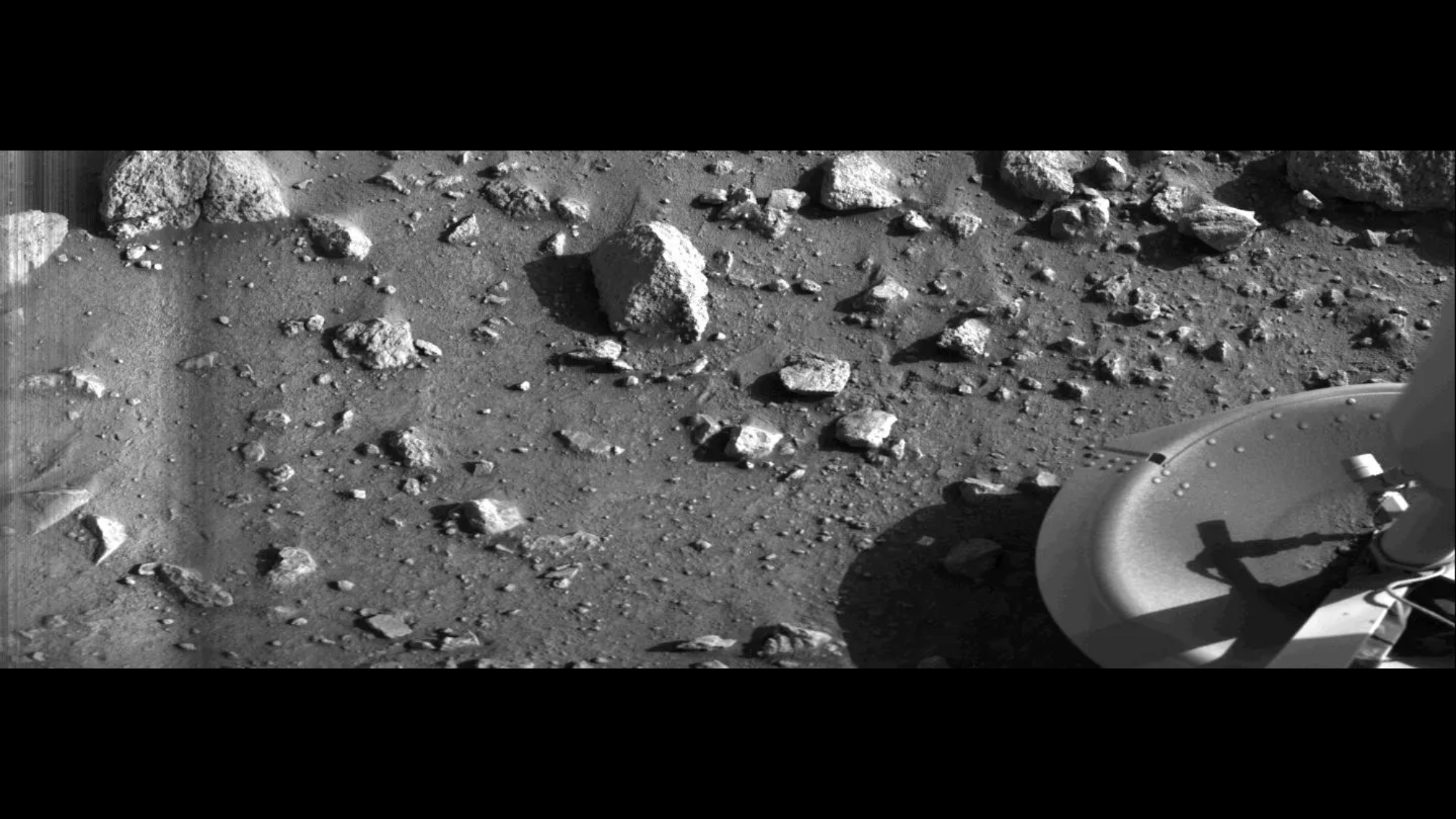 A black-and-white image of the surface of Mars with rocks and part of the Viking 1 lander. 