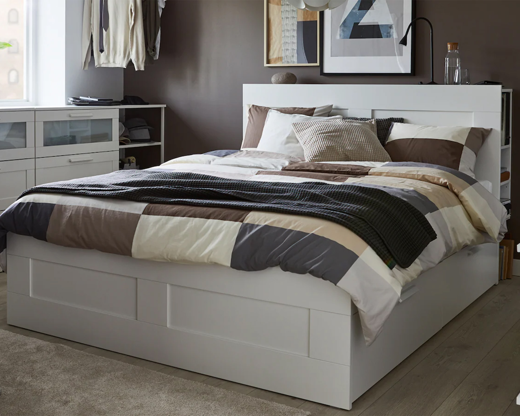 A bedroom with chocolate brown wall decor, a bed with in-built shelf and drawers and open clothes rail