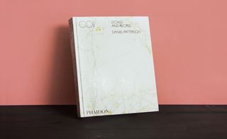 Front cover of the book 'Coi: Stories and Recipes', white cover, branch design with yellow flowers and black lettering, dark wood surface, orange background