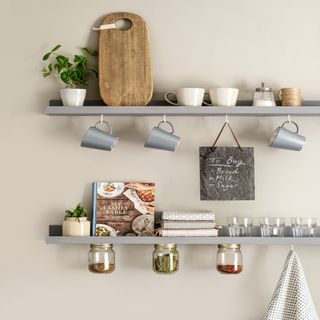 grey shelves with hooks containing mugs, mini blackboard, wooden chopping board, plant