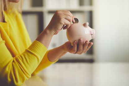 Woman puts coins in a piggy bank to save up
