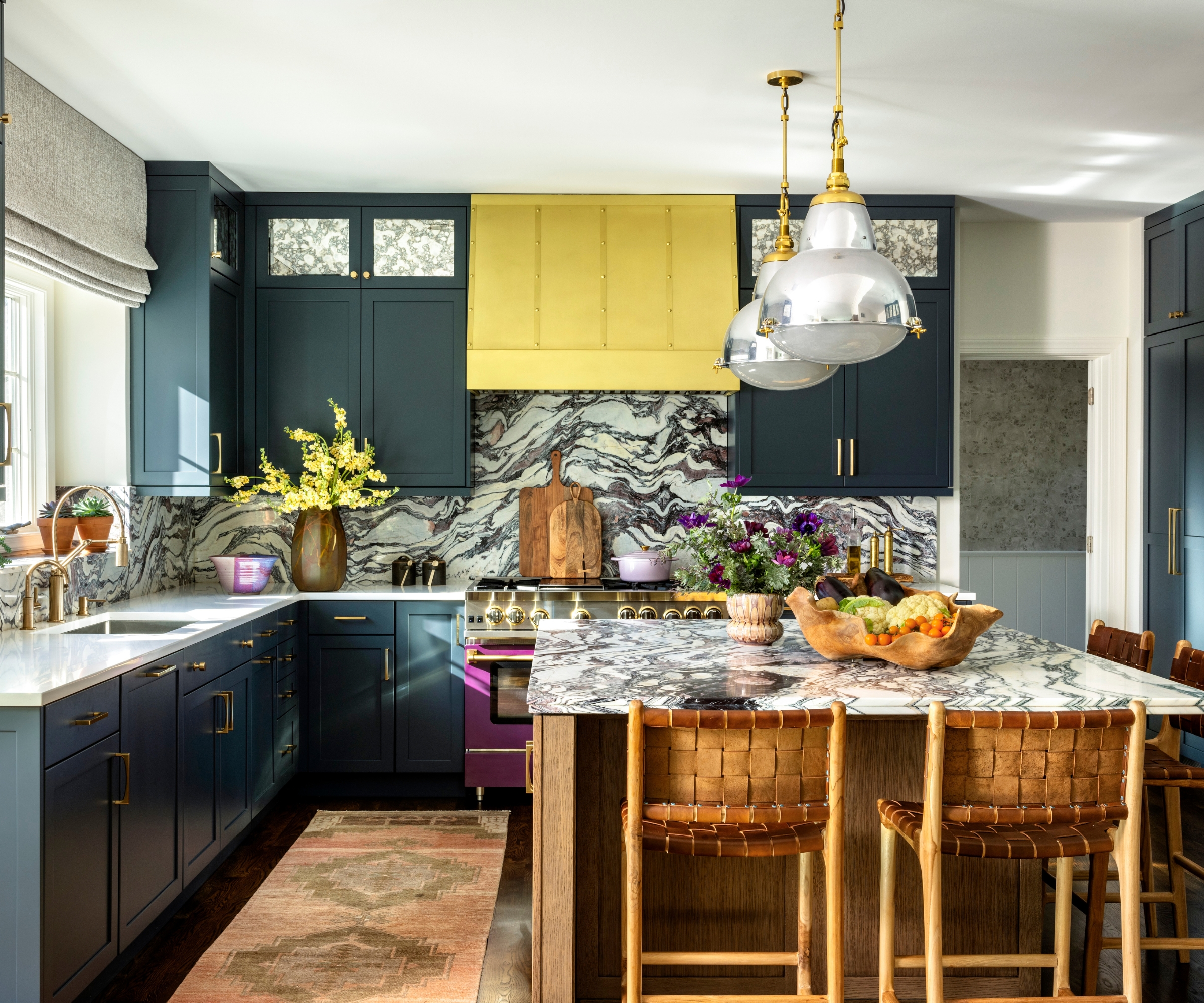 a large kitchen with navy cabinetry, marble countertops and backsplashes, a yellow range hood, and a pink range