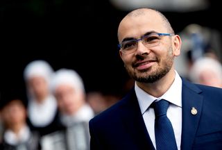 Demis Hassabis, Google DeepMind CEO - A shot of Hassabis in the foreground wearing a suit, with a heavily blurred crowd in the background