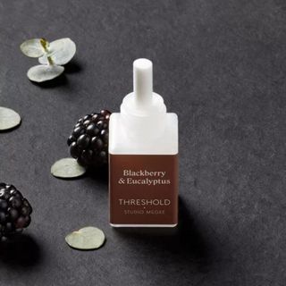 A small Pura fragrance bottle surrounded by blackberries and eucalyptus leaves