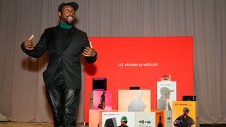 Will.i.am speaking about XBoom speakers at CES 2025, wearing all black with a black cap