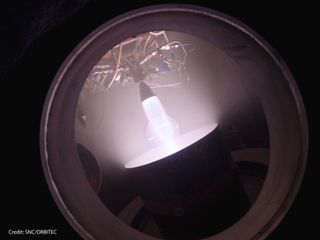 A prototype thruster for Sierra Nevada's Dream Chaser space plane undergoes testing in a vacuum chamber to simulate the orbital environment.
