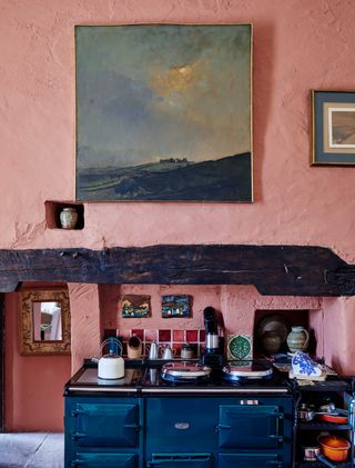 kitchen painted pink with dark blue aga and beam mantlepiece