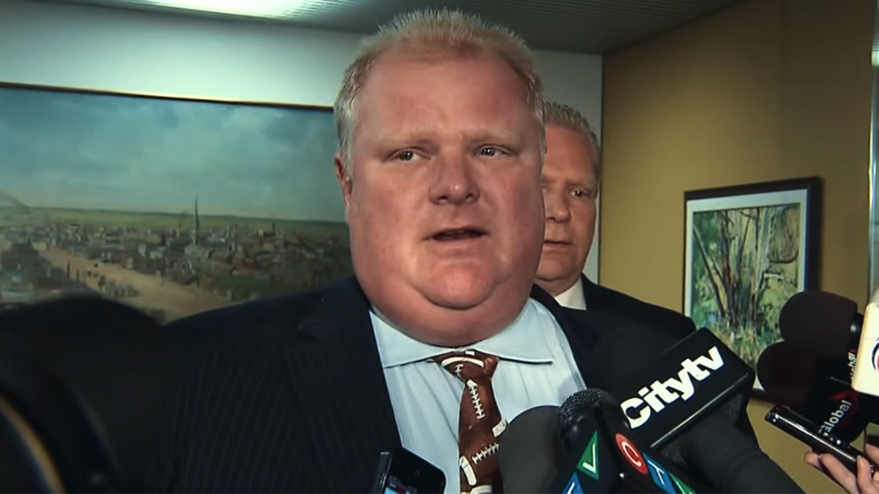Rob Ford in a press conference with microphones in front of him in Trainwreck: Mayor of Mayhem