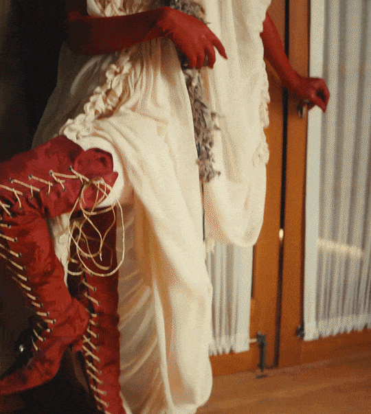 gif of natasha lyonne leaning back against a wall wearing red stockings, red gloves, and a floaty yellow dress
