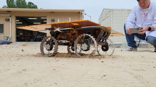 a small four-wheeled rover travels across sand in a test yard at nasa's jet propulsion laboratory.