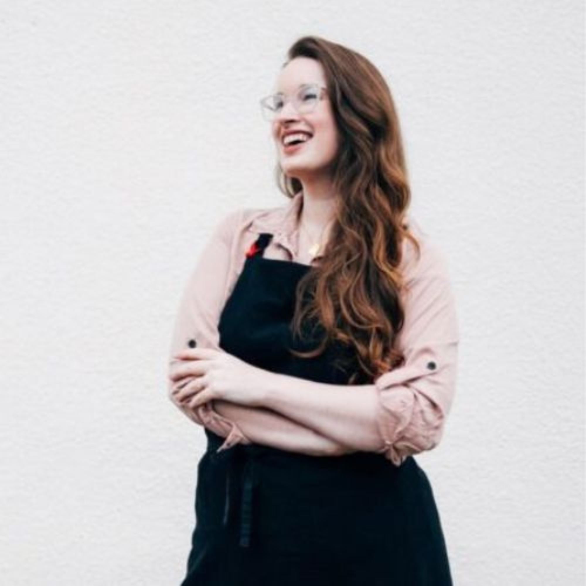 Emily Laurae in apron standing against white wall