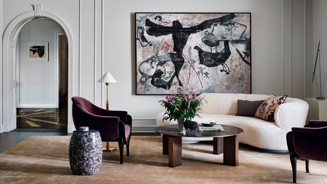 white living room with white curved sofa, brown round coffee table, purple armchair and statement artwork 