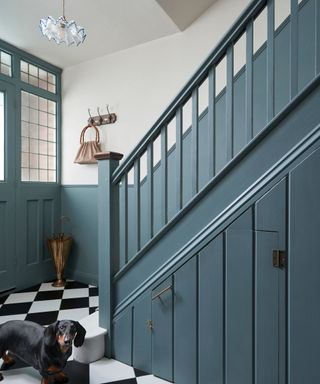 entryway with muted blue staircase and lower walls and front door, white upper wall and black and white tiled floor