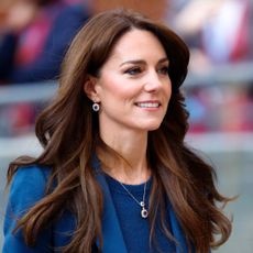 Kate Middleton has long wavy brunette hair and is wearing a royal blue suit