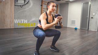 Woman in gym holds dumbbell as she squats