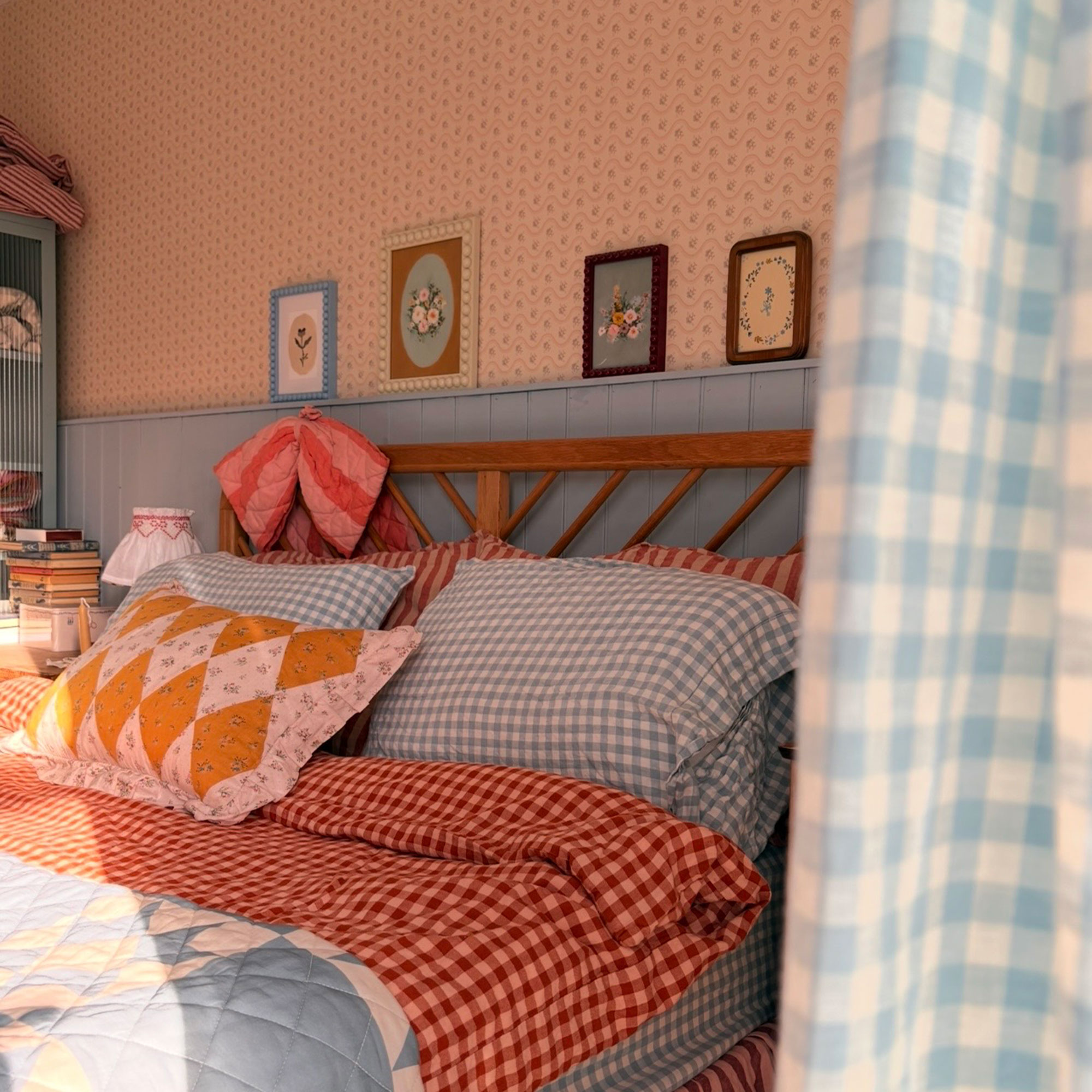Bedroom with walls half pink patterned wallpaper and half blue panelling with bed dressed in blue and red gingham linens