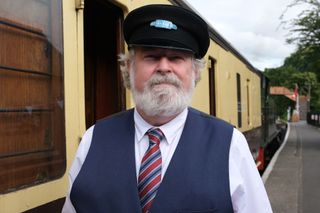 Noah Culpepper (Paul Bradley) stands next to the carriages of a vintage steam train. He is wearing a guard's outfit, his costume for the play.