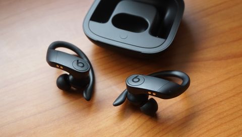 The Beats Powerbeats Pro buds pictured next to their charging case on a wooden surface