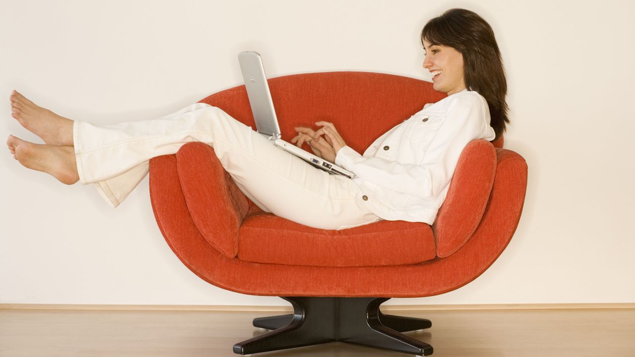 Woman sitting on orange seat with laptop and laughing