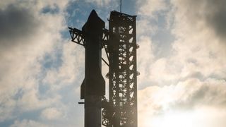 A SpaceX Starship rocket atop its booster at launchpad with clouds overhead