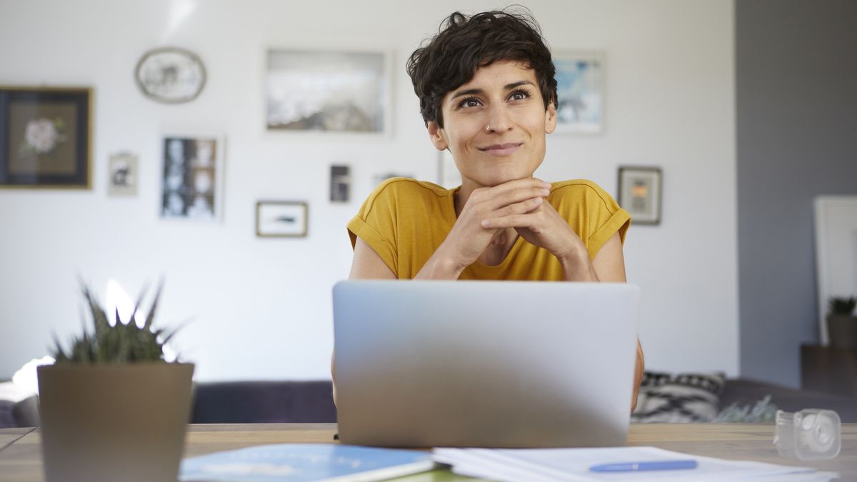 How to create a healthy home office setup: A woman with short dark hair looks happy sat at her home office desk