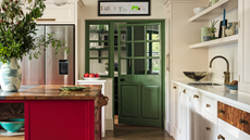 a kitchen with a red kitchen island, white cabinets, open shelves, and a green pantry door