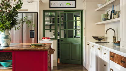 a kitchen with a red kitchen island, white cabinets, open shelves, and a green pantry door
