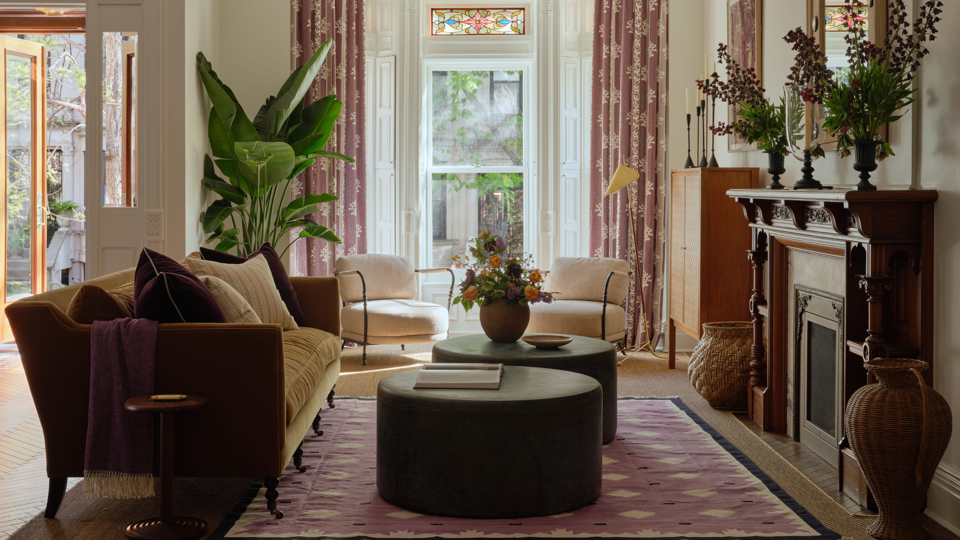 the living room of a Park Slope townhouse in New York with huge bay window with stain glass, antique wooden fireplace, and modern furnishings