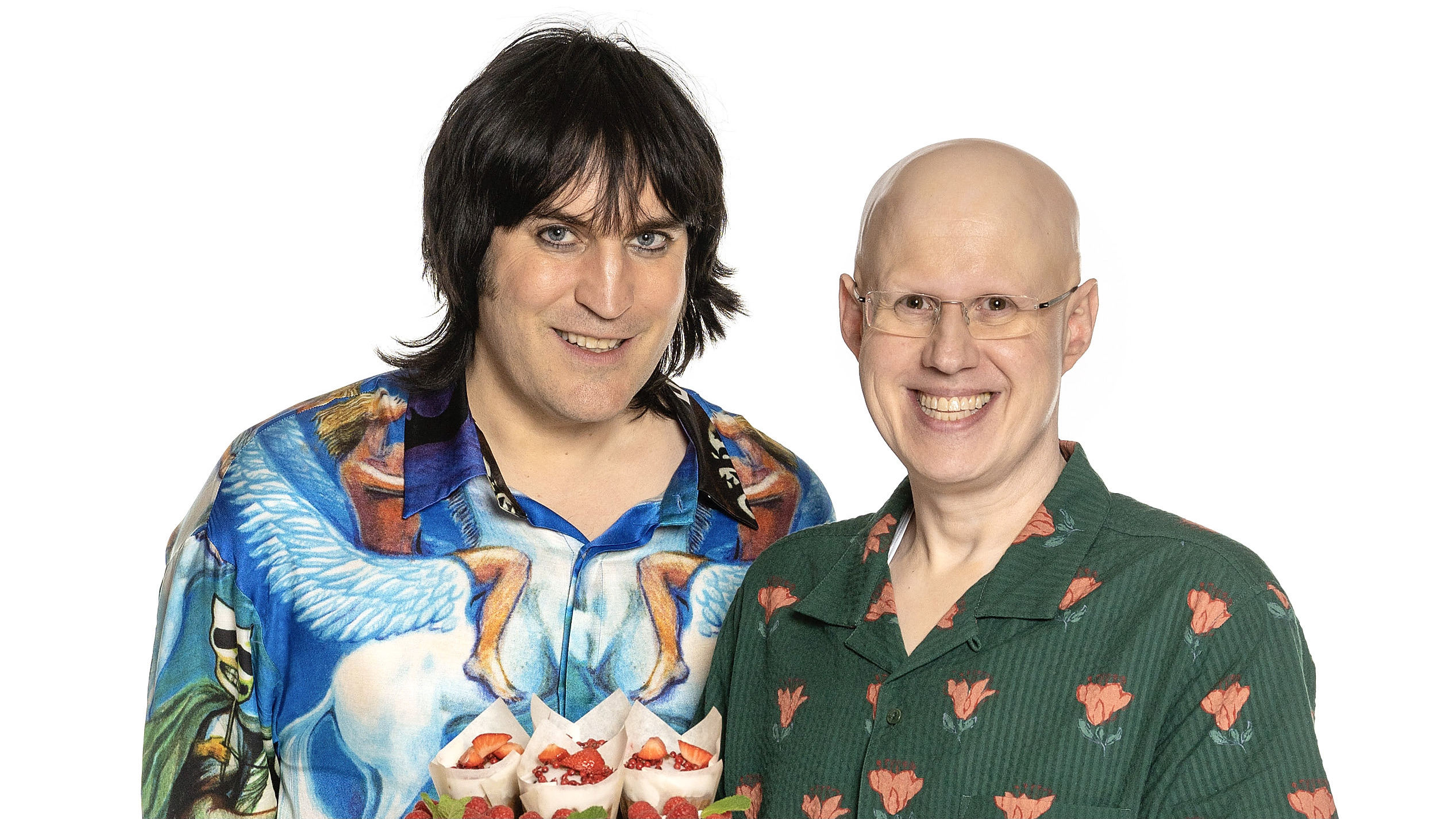 Noel Fielding in a blue printed shirt and Matt Lucas in a green printed shirt hold some strawberry-topped cakes in The Great British Bake Off.