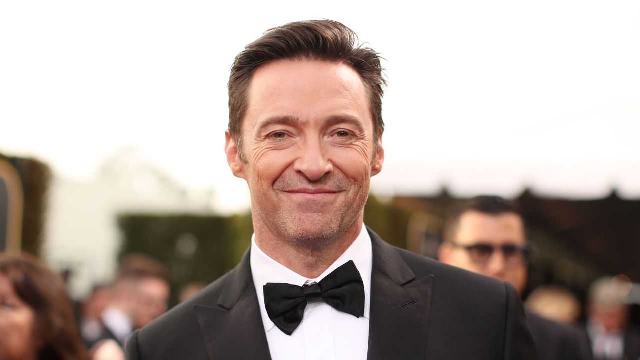 hugh jackman wearing a suit on a white background with people behind him