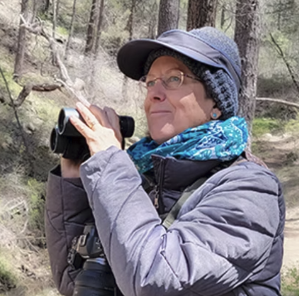 woman wearing blue anorak and hat holding binoculars