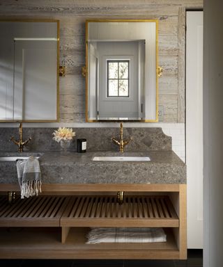 A bathroom backsplash idea with brown stone extended vanity surface, wooden walls and double mirrors