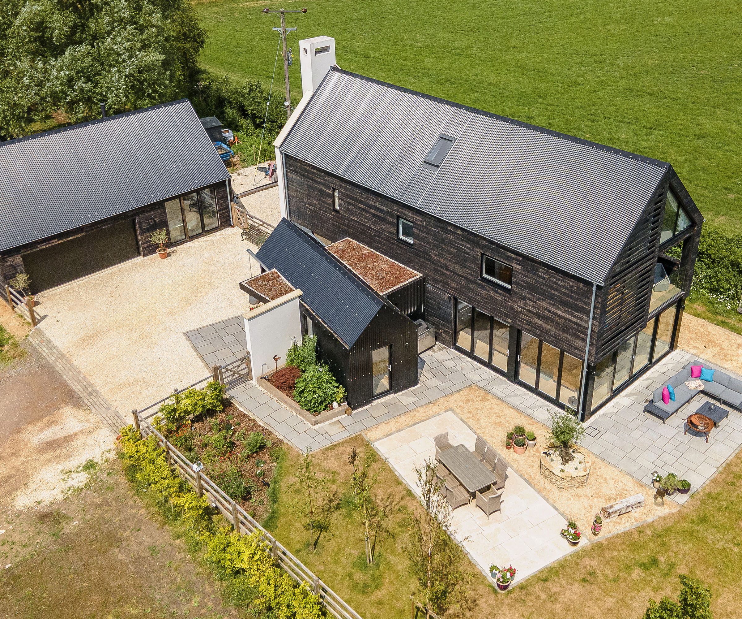 An aerial drone shot of a self build home with additional outbuilding and landscaped outdoor seating areas