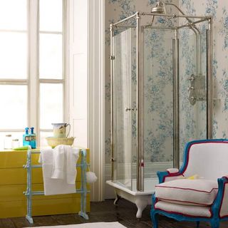 Vintage bathroom with blue and white floral wallpaper, a freestanding shower, blue, white and red armchair and yellow cupboard