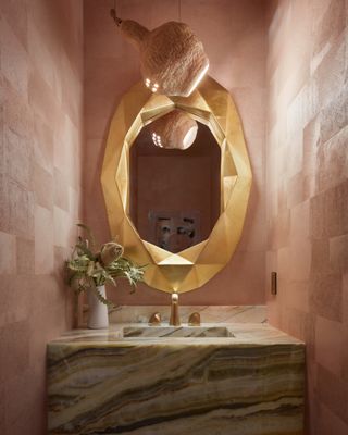 Small powder room with pink textured wallpaper, a gold mirror and light