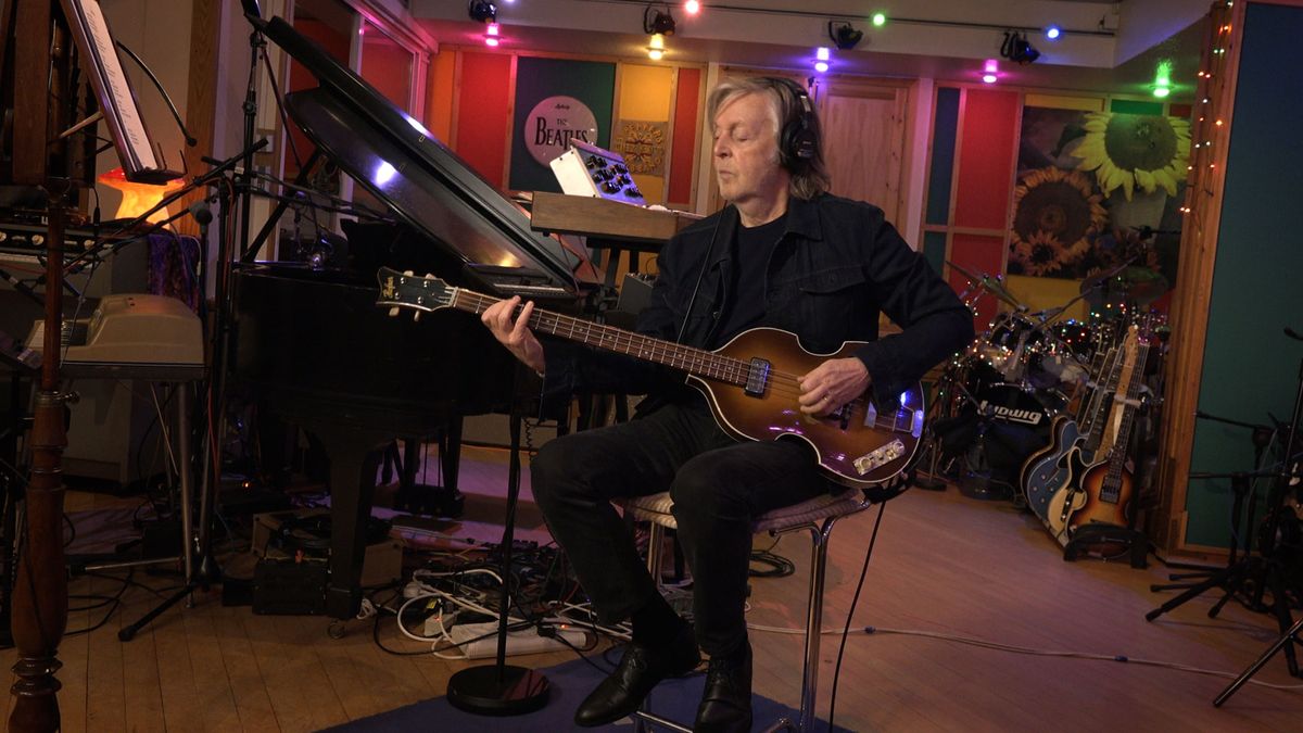 image of Sir Paul McCartney playing the guitar, creating Now and Then song. Behind him is Beatles memorabilia and guitars