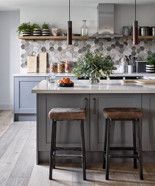 Gray, beige and white stone hexagonal kitchen wall tile ideas in a classic gray kitchen scheme, with wooden flooring and a breakfast bar.