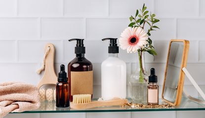 a clear floating bathroom shelf with skincare and a vase with a flower on a white tiled wall