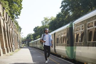 Young man walking along a platform on a sunny day, having just got off a train