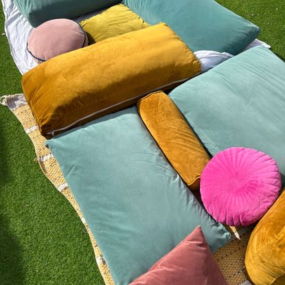 Pile of gold, teal and pink cushions on grass