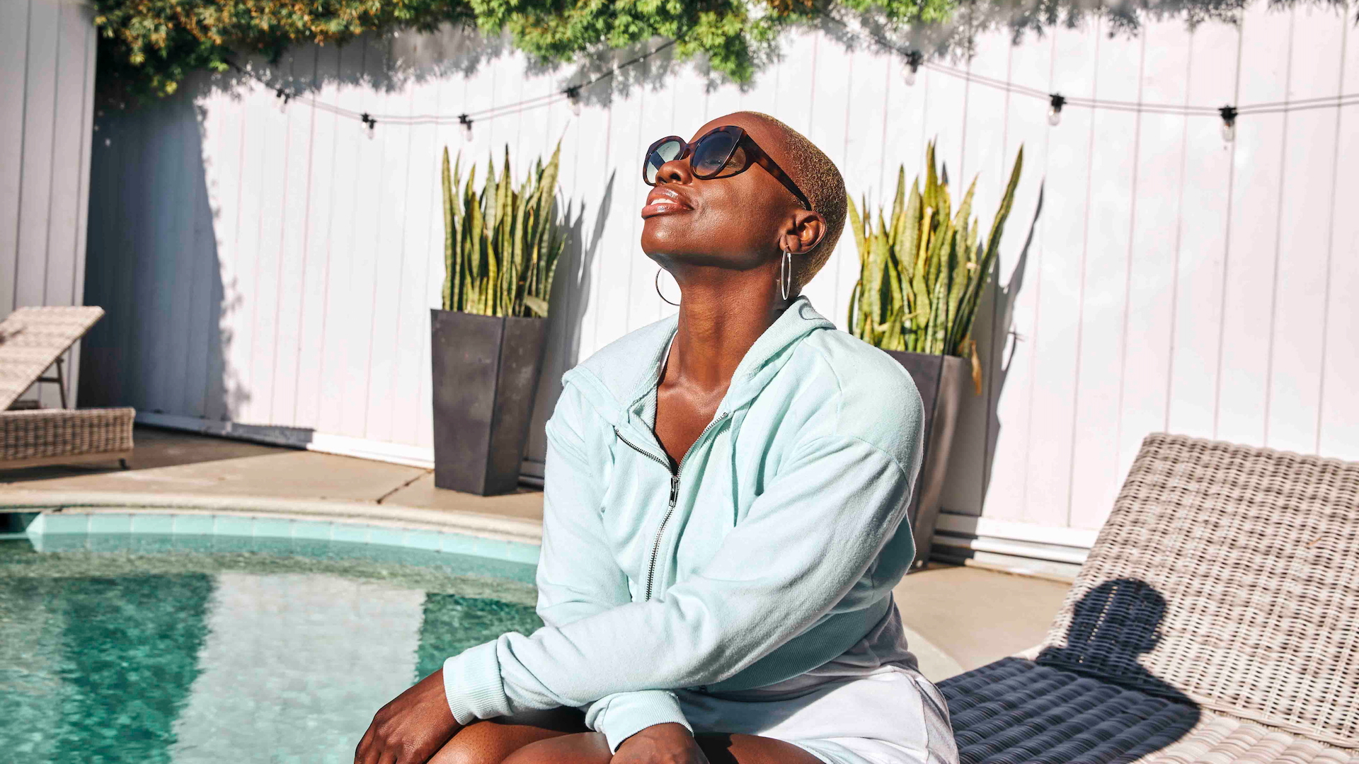 A woman sits on a sunlounger beside a pool