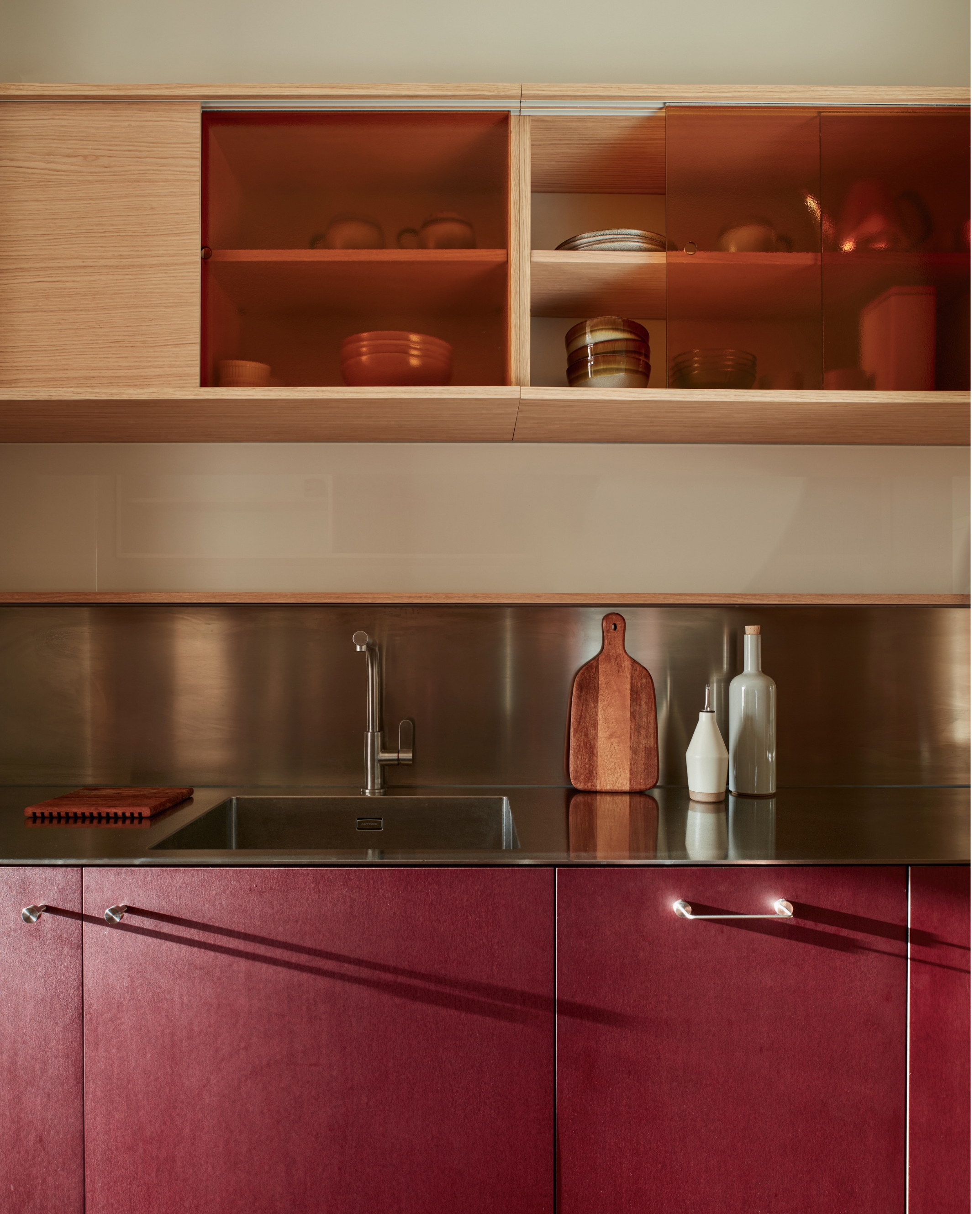 Plum colored kitchen cabinets with stainless steel worktops and wooden cabinets above the sink.