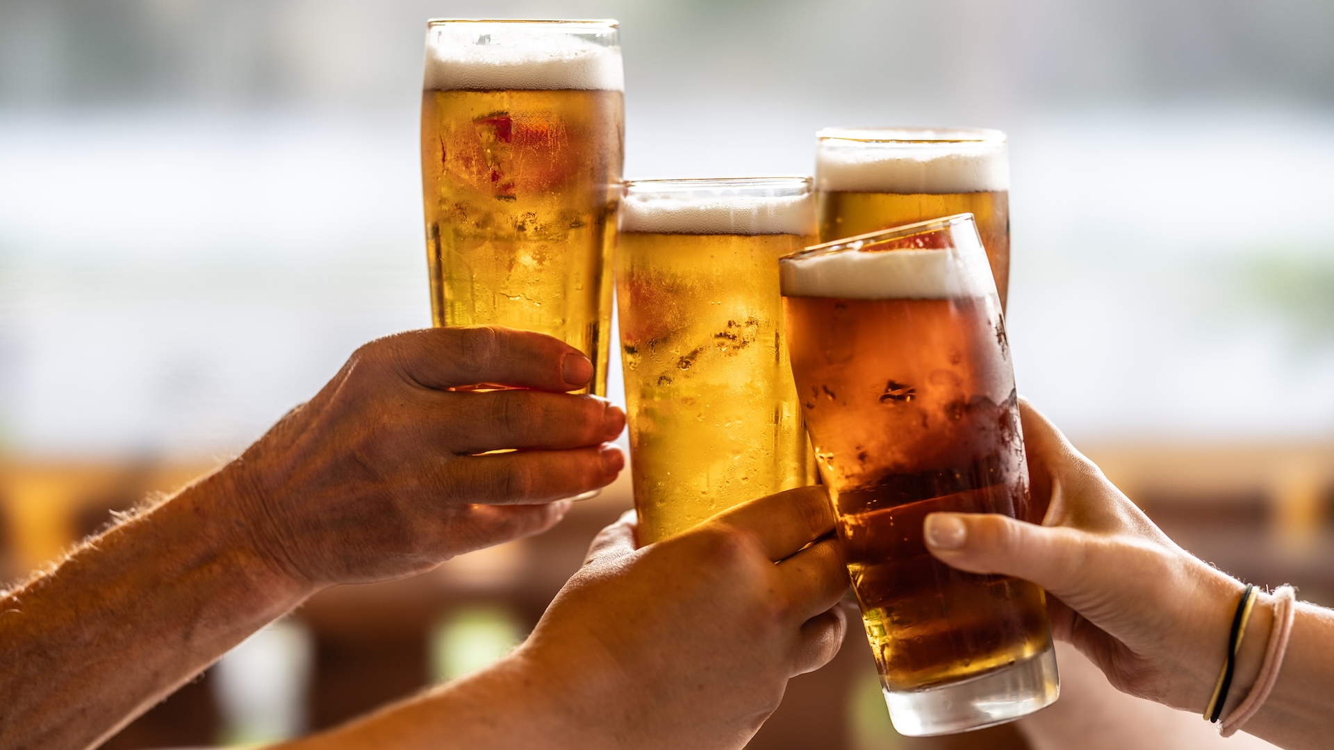 Group of friends toasting with beer on the terrace during hot summer days. Close-up of a group of people clinking glasses with beer