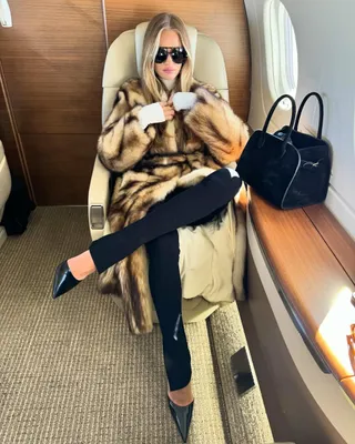 Model Rosie Huntington-Whiteley wears black leggings, black flats, The Row Margaux bag, and a leopard fur coat while sitting on a private plane.