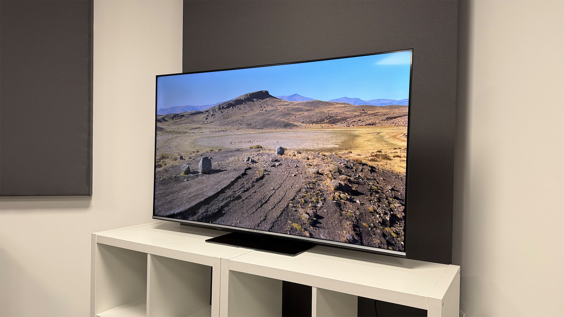 Mitchell &amp;amp; Brown QLED1811 QLED TV on white shelving unit, on screen is dirt road