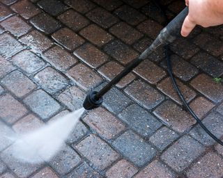 person cleaning block paving with a pressure washer